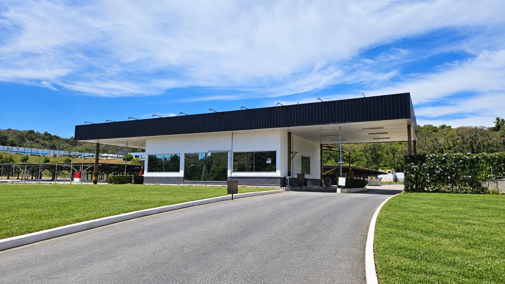Entrance building of Bandeira Park Confins, with a black canopy, a paved driveway and a lawn, on the MG-010 highway in Vespasiano (MG)